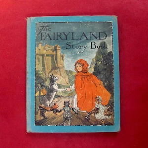 May include: A vintage copy of "The Fairyland Story Book" with a blue cover. The cover illustration shows a girl in a red cape, a castle, and various animal characters. The background features a mountain range, creating a fairytale scene.