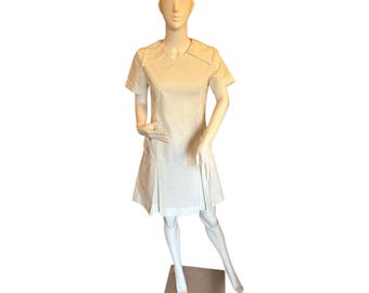 May include: A white short-sleeved dress with a V-neck and a pleated skirt. The dress is on a white mannequin.