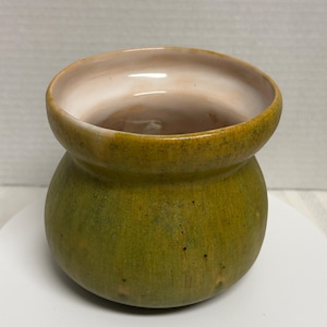 May include: A handcrafted ceramic pot with a bulbous base and a flared rim. The exterior is a mottled olive green, while the interior and rim are a creamy off-white. The pot has a rustic, organic aesthetic, suitable for small plants or decorative use.