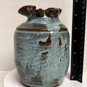 May include: A handcrafted ceramic vase with a unique ruffled rim. The vase features a blend of blue and brown glaze, creating a textured, organic appearance. The vase is approximately 6 inches tall.