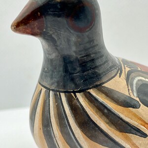May include: A ceramic bird figurine with a black head and neck, a brown beak, and a body adorned with brown, tan, and black stripes. The bird has a detailed painted design and a glossy finish, showcasing a handcrafted aesthetic.