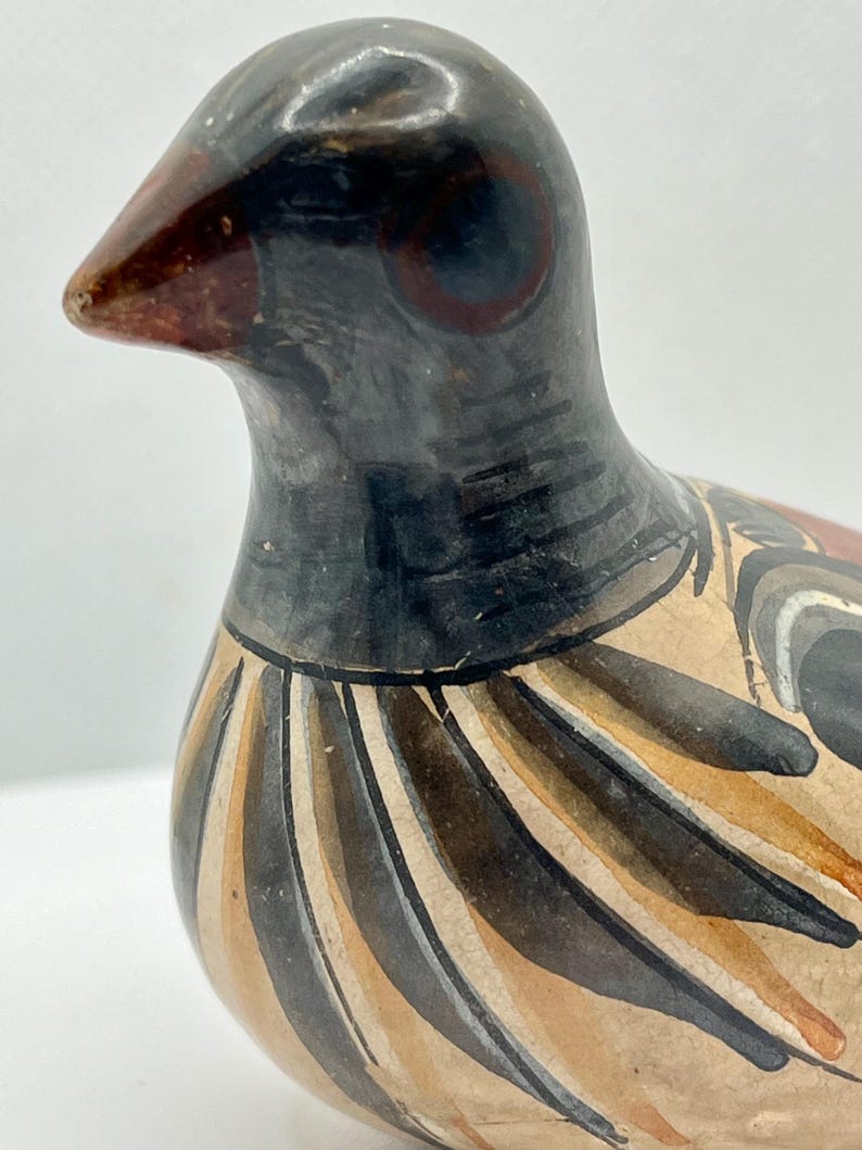 May include: A ceramic bird figurine with a black head and neck, a brown beak, and a body adorned with brown, tan, and black stripes. The bird has a detailed painted design and a glossy finish, showcasing a handcrafted aesthetic.