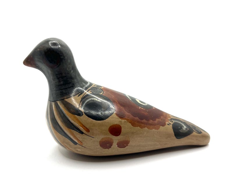 May include: A ceramic bird figurine with a black head and neck, and a body painted with brown, tan, and black details. The bird is in a resting position, with its beak slightly open. The figurine is a decorative item.