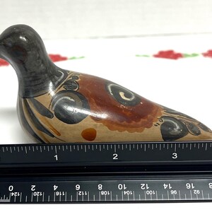 May include: A ceramic bird figurine, hand-painted with brown, black, and tan colors. The bird's body is approximately 4 inches long. Decorative swirls and patterns adorn the bird's body. The bird is positioned on a white surface.