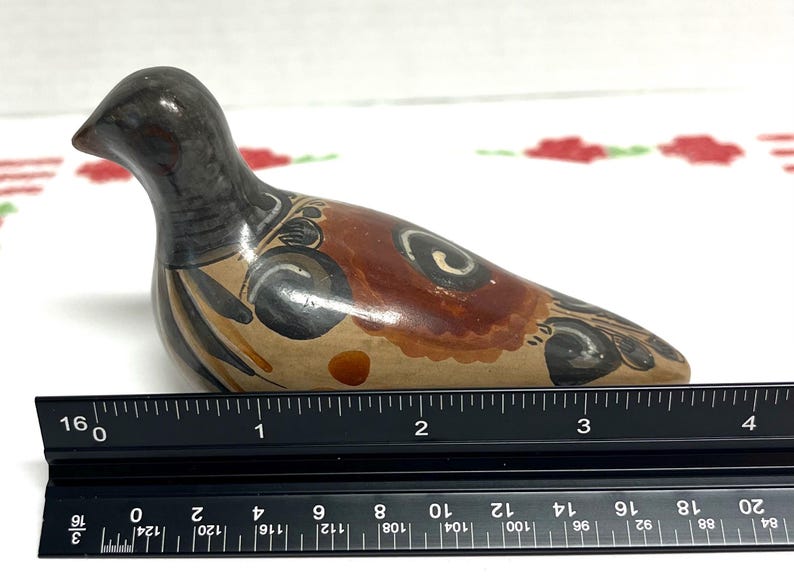 May include: A ceramic bird figurine, hand-painted with brown, black, and tan colors. The bird's body is approximately 4 inches long. Decorative swirls and patterns adorn the bird's body. The bird is positioned on a white surface.