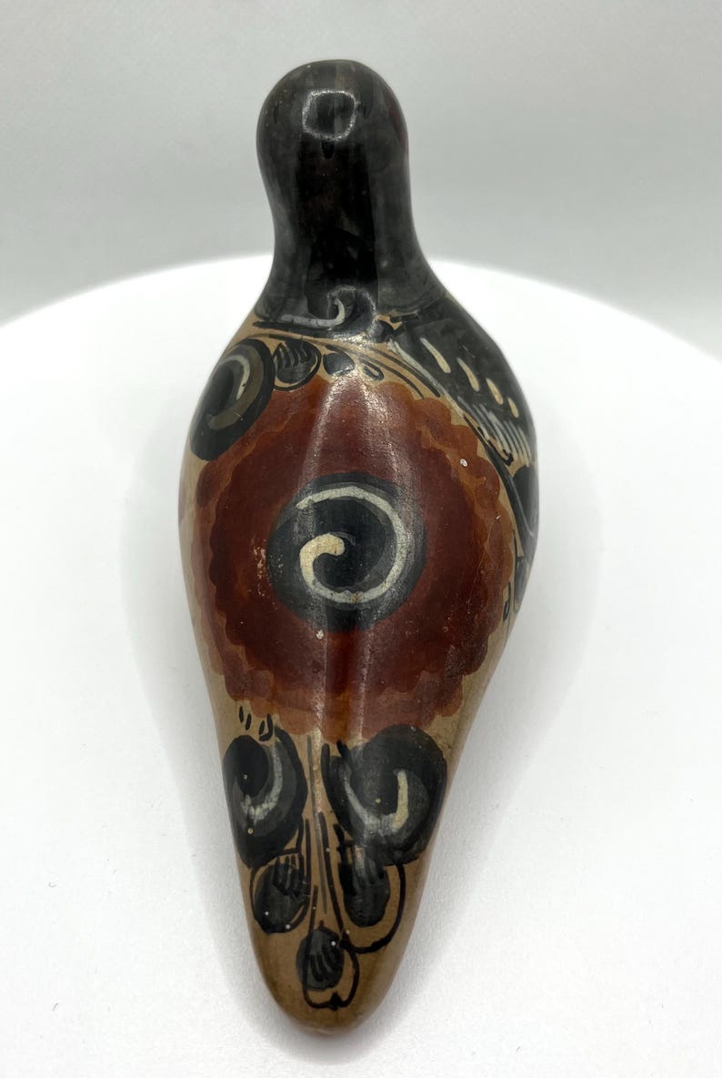 May include: Hand-painted ceramic vessel with a teardrop shape. The top is black, transitioning to a tan body with a central maroon floral design and black and white accents. The vessel is likely for decorative use.