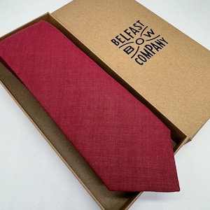 Könnte beinhalten: Eine burgunderfarbene Krawatte aus Leinen in einer braunen Schachtel mit dem Aufdruck "BELFAST BOW COMPANY" auf der Schachtel.