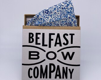 May include: A brown box with the text "Belfast Bow Company" printed in black. The box contains a white and blue floral patterned fabric.