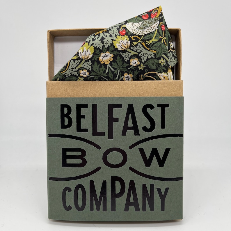 May include: A green box with the text "BELFAST BOW COMPANY" printed on the front. The box contains a green and brown patterned pocket square with a bird and floral design.