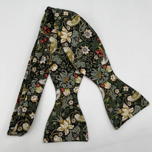 May include: A green bow tie with a floral pattern featuring birds and berries. The pattern is reminiscent of vintage wallpaper.