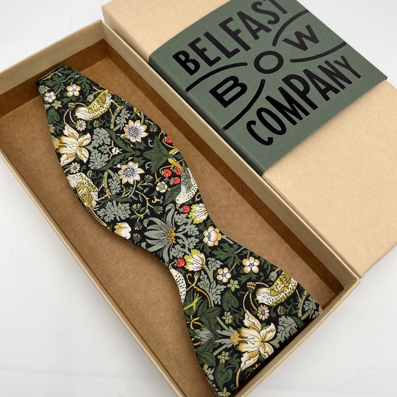 May include: A green, black, white, and red bow tie with a floral pattern. The bow tie is in a brown box with the text "BELFAST BOW COMPANY" on the lid.