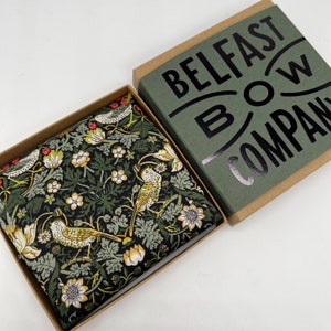 May include: A green and black patterned bow tie with a floral design and birds. The bow tie is in a box with the text "Belfast Bow Company" on the lid.