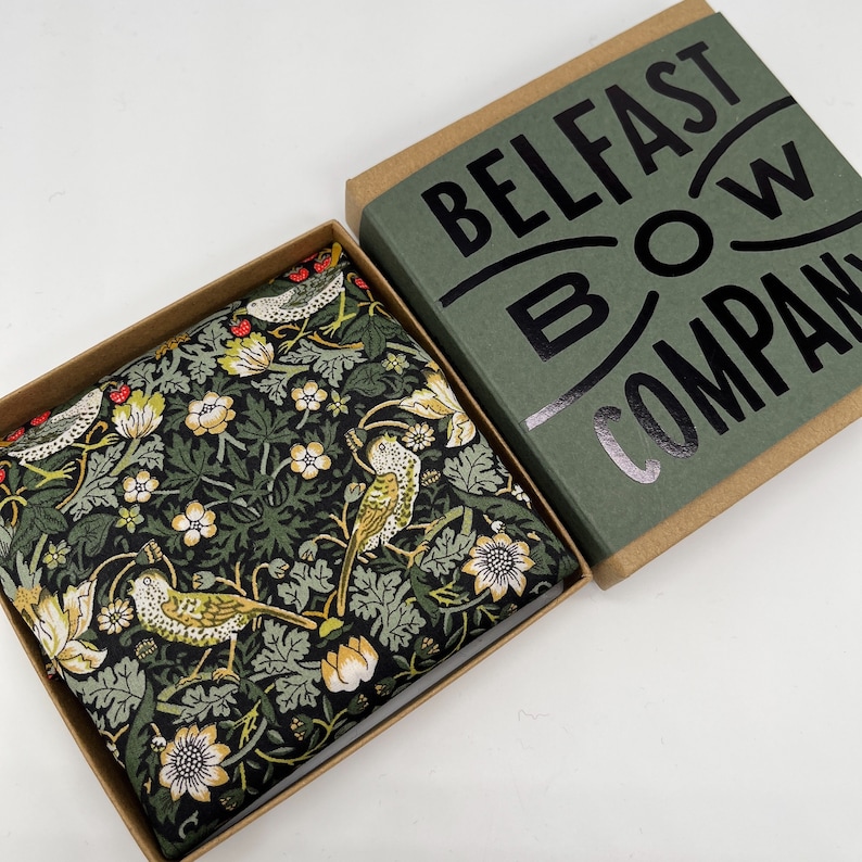 May include: A green and black patterned bow tie with a floral design and birds. The bow tie is in a box with the text "Belfast Bow Company" on the lid.