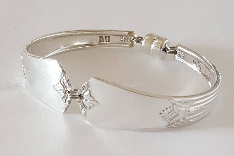 Peut inclure: Bracelet en argent fabriqu&eacute; &agrave; partir d'une cuill&egrave;re r&eacute;utilis&eacute;e avec un motif d&eacute;coratif et un fermoir magn&eacute;tique. La cuill&egrave;re porte les marques "S1" et "SK" au dos.