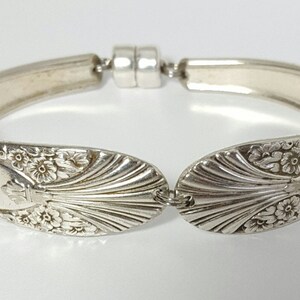 May include: A silver bracelet made from a repurposed spoon with a floral design and a magnetic clasp.