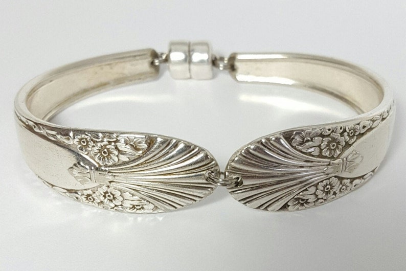 May include: A silver bracelet made from a repurposed spoon with a floral design and a magnetic clasp.