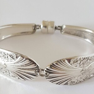 May include: Silver bracelet crafted from a vintage spoon featuring a floral design. The bracelet is open and has a magnetic clasp.