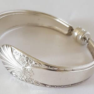 May include: A silver bracelet made from a repurposed spoon with a floral design. The bracelet has a magnetic clasp.