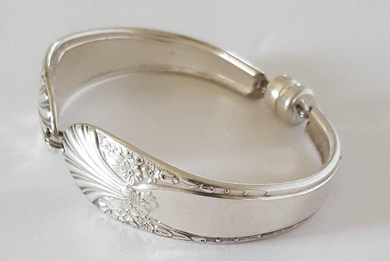 May include: A silver bracelet made from a repurposed spoon with a floral design. The bracelet has a magnetic clasp.
