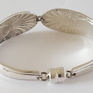 May include: Silver spoon bracelet with a floral design and a magnetic clasp.