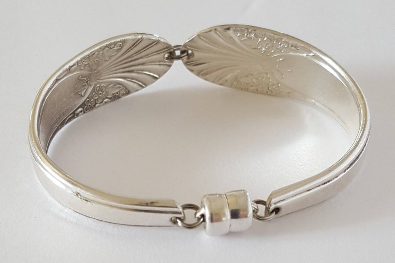 May include: Silver spoon bracelet with a floral design and a magnetic clasp.
