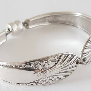 May include: A silver bracelet made from a repurposed spoon. The spoon features a floral design and is secured with a magnetic clasp.