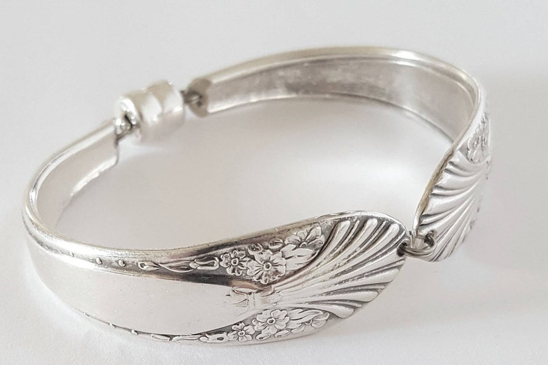 May include: A silver bracelet made from a repurposed spoon. The spoon features a floral design and is secured with a magnetic clasp.