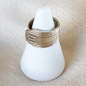 May include: A silver ring made from a repurposed spoon with an Art Deco design. The ring is displayed on a white ring holder.