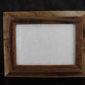 May include: A rectangular picture frame constructed from weathered brown wood with a visible grain pattern. The frame features mitered corners and a wide, flat border surrounding a plain, off-white rectangular center panel.