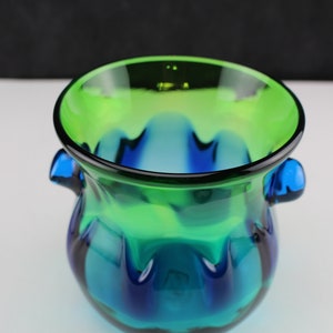May include: A green and blue glass vase with two handles. The vase has a wavy, textured design.