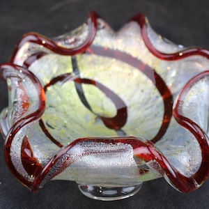 May include: A clear glass bowl with a wavy rim and a swirl design in red and silver.
