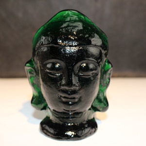 May include: A green glass sculpture of a Buddha head. The head is black and the face has a serene expression.