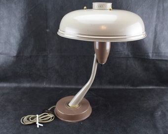 May include: A mid-century modern desk lamp with a beige metal shade and a brown metal base. The lamp has a flexible arm and a cord.