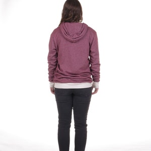 May include: A woman wearing a maroon hoodie with a white undershirt and black jeans. She is standing with her back to the camera.
