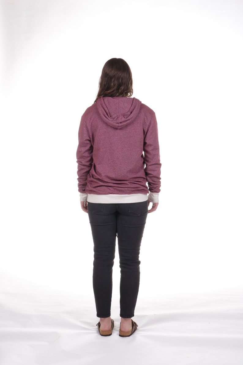May include: A woman wearing a maroon hoodie with a white undershirt and black jeans. She is standing with her back to the camera.