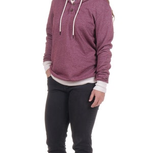 May include: A woman wearing a maroon hoodie with a white trim and a button closure. She is wearing black jeans and brown sandals.