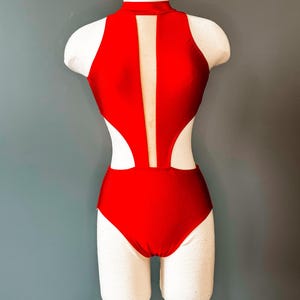 Könnte beinhalten: Ein roter Tanzanzug mit hohem Ausschnitt und Cut-Out-Design. Der Tanzanzug hat eine transparente Einsätze im Rücken.