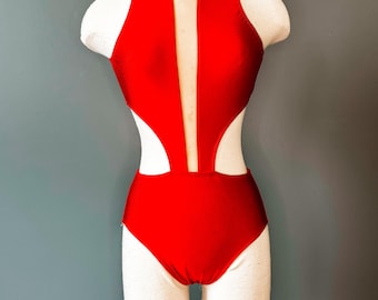 May include: A red leotard with a high neckline and a cutout design. The leotard has a sheer panel in the back.