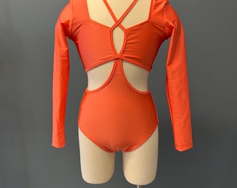 May include: A coral-colored leotard with long sleeves and a criss-cross design in the back. The leotard has cutouts on the sides and back.