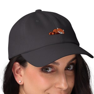 Può includere: Un cappello da baseball nero con un design di panda rosso ricamato. Il panda è sdraiato e ha un petto bianco e occhi neri.