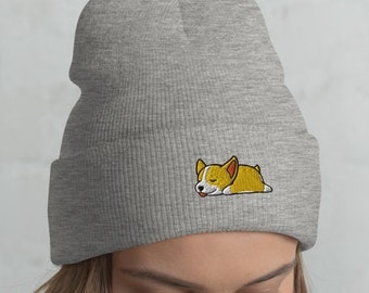 May include: A gray beanie with a cute embroidered cartoon corgi sleeping on it. The beanie is made of a soft, warm material and is perfect for keeping your head warm in the winter.