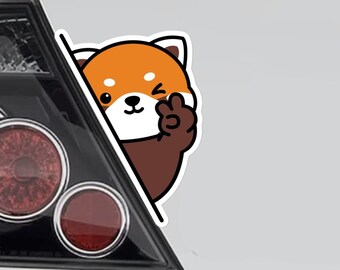 Puede incluir: Dos pegatinas de panda rojo en un coche blanco. Los pandas rojos asoman por detrás de una esquina y hacen un signo de paz.