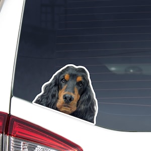 Puede incluir: Una pegatina de un perro Cocker Spaniel negro y fuego con pelo largo y ondulado. La pegatina está colocada en la ventana trasera de un vehículo blanco, mostrando la cabeza y los hombros del perro. El perro tiene una expresión apacible.