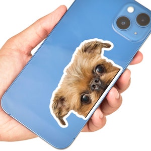 Peut inclure: Une coque de t&eacute;l&eacute;phone bleu avec un autocollant repr&eacute;sentant un griffon bruxellois brun qui d&eacute;passe de la coque.