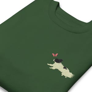 May include: A dark green sweatshirt with a white and black embroidered image of a dog chasing a pink butterfly.