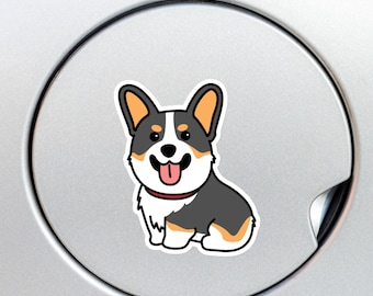 May include: A cartoon corgi dog sticker with a cheerful expression. The corgi has black, white, and tan fur, a red collar, and a pink tongue. The sticker is on a silver surface.