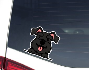 May include: A black Schnauzer dog sticker with a white outline, peeking over a white line. The dog has pink inner ears and a pink tongue sticking out. The sticker is affixed to a car window.