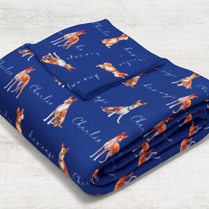May include: A blue fleece blanket with a repeating pattern of a brown and white dog with the name "Charlie" written in white script.