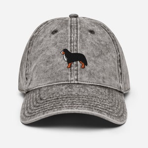 May include: A gray distressed denim baseball cap with an embroidered black and white Bernese Mountain Dog.