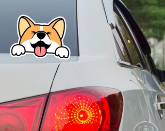 May include: A car window sticker featuring a cartoon corgi dog with a happy expression. The corgi has orange and white fur, a black nose, and a pink tongue sticking out. The sticker is applied to the rear window of a white car.